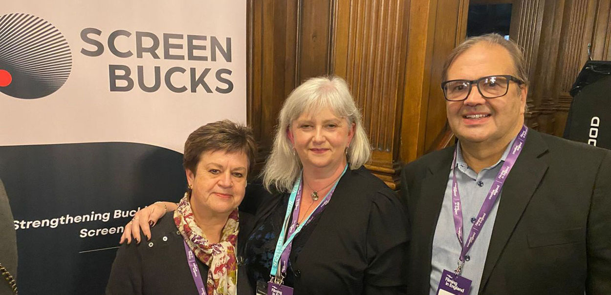 Three people standing together in front of Screen Bucks sign